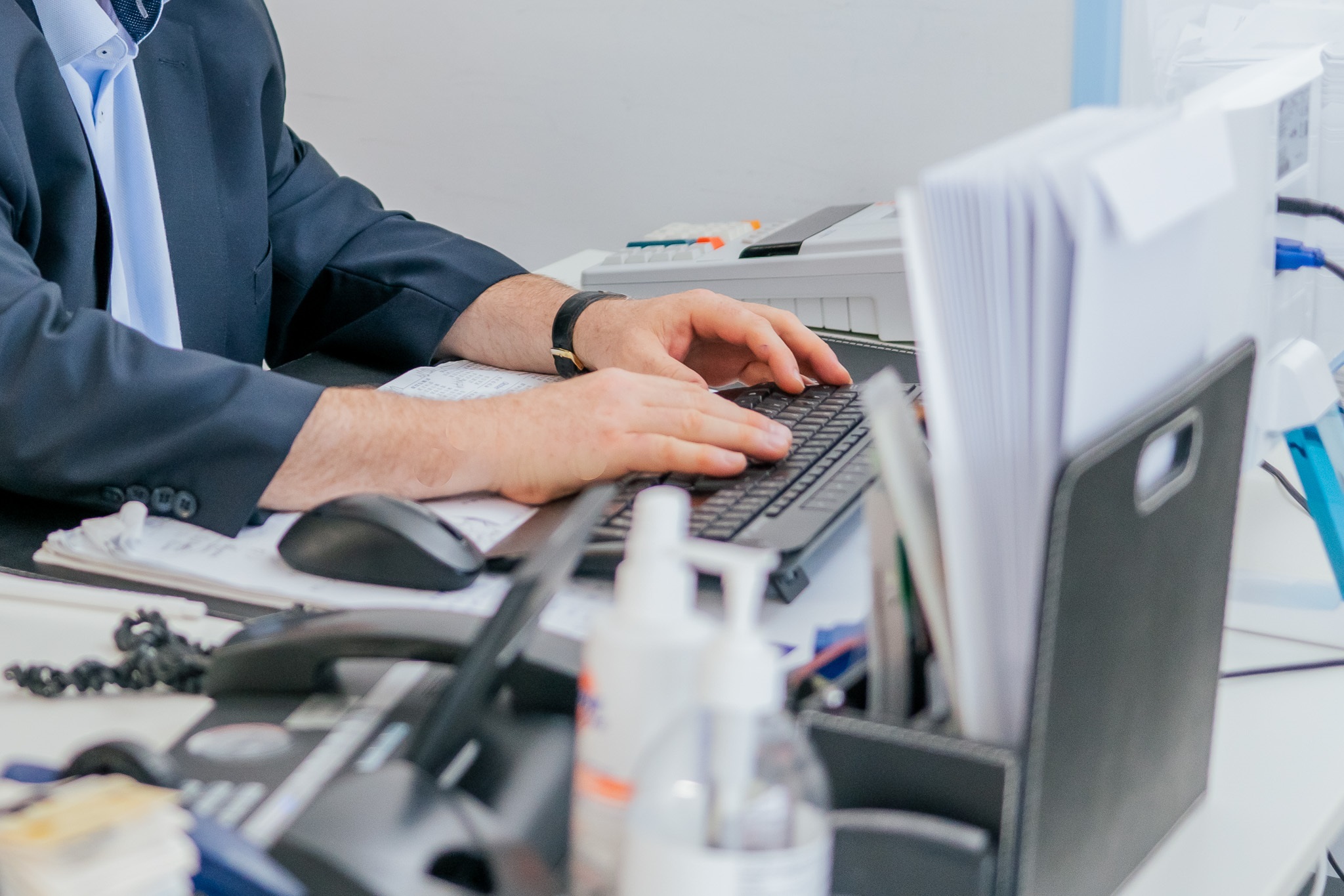 Ein Mann im Anzug tippt konzentriert auf einer schwarzen Tastatur im Büro